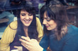 © Dangubic - Two girls smiling and using smart phone in a cafe