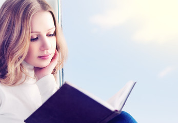 Poster - beautiful young woman reading a book while sitting at a window