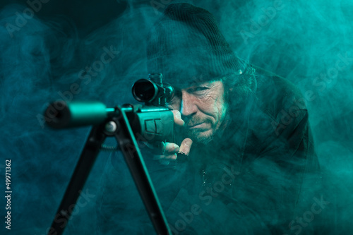 Fotografía Sniper with beard in black holding gun. Studio shot.