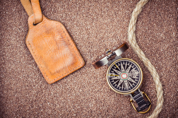 Vintage compass and leather tag on sand background