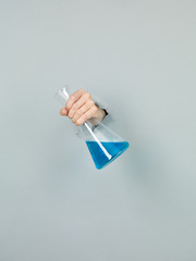 Wall Mural - close-up of femal hand holding a chemistry flask with blue liqui