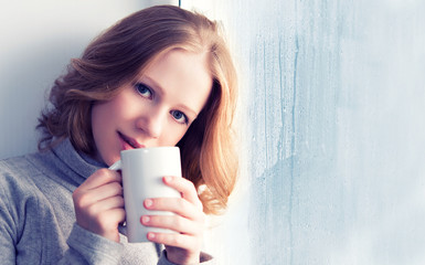 Poster - beautiful dreamy young woman with a cup of hot coffee at the win