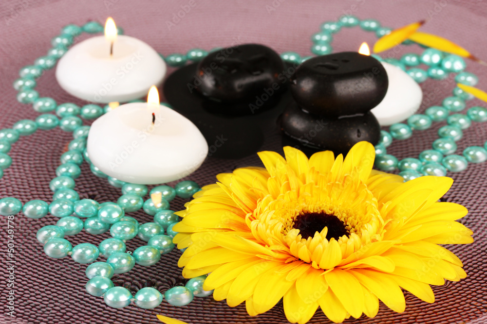 spa stones with flower and candles in water on plate