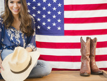 Hispanic Woman Holding Cowboy Hat And Sitting Next To American Flag