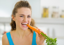 Happy Young Woman Eating Carrot In Kitchen