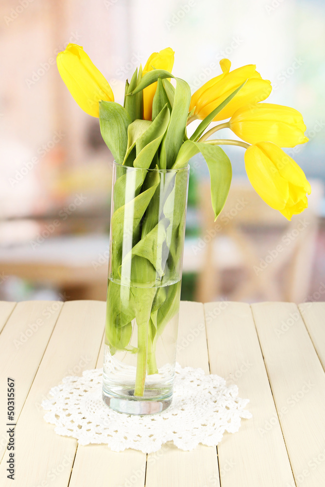 Yellow tulips in vase on wooden table on room background