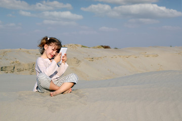 Wall Mural - little girl sitting on sand and play with tablet pc