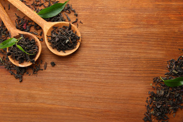 Dry tea with green leaves in wooden spoons, on wooden