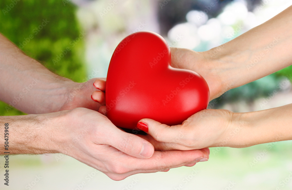 Red heart in woman and man hands, on green background
