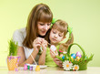 mother and child girl paint easter eggs over green background