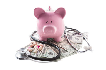 Piggy bank tablets stethoscope resting on pile of dollars