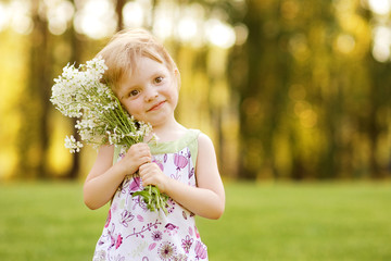 nice little girl with flowers on the grass in summertime