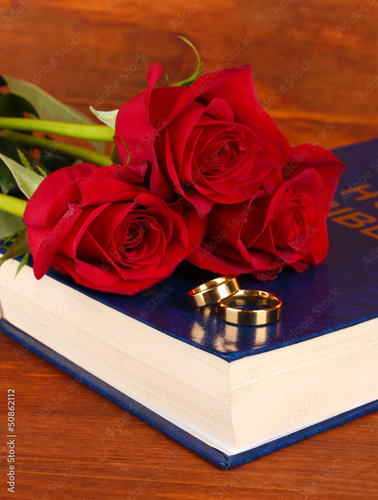 Wedding rings on bible with roses on wooden background