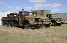 Three Old Army Vehicles Parked In A Grass Field