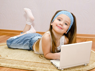 Wall Mural - Smiling little girl with a laptop at home on the floor