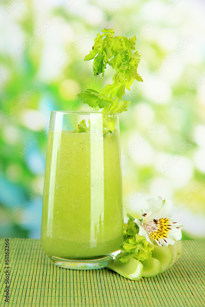 Glass of celery juice, on bamboo mat, on green background