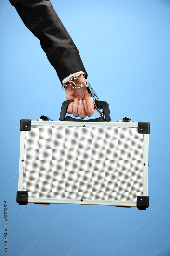 Hand with handcuff and suitcase, on color background