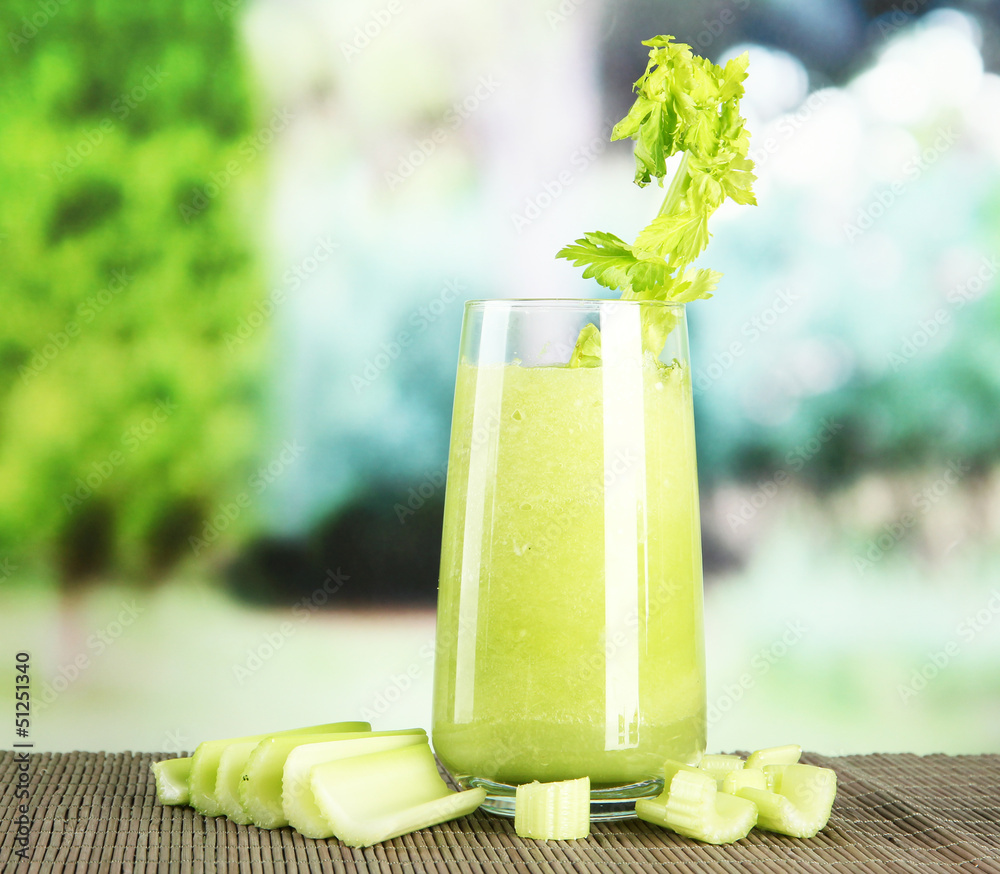 Glass of celery juice, on bamboo mat, on green background