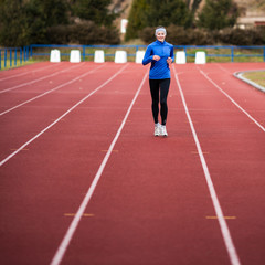 Wall Mural - Young woman running at a track and field stadium