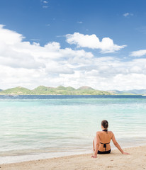 Poster - Young beautiful woman is sitting on sand by the sea