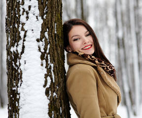 Beautiful brunette leaning on a tree trunk in the winter