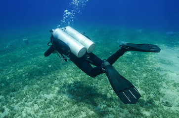 girl scuba dives in clear blue water with twin tanks