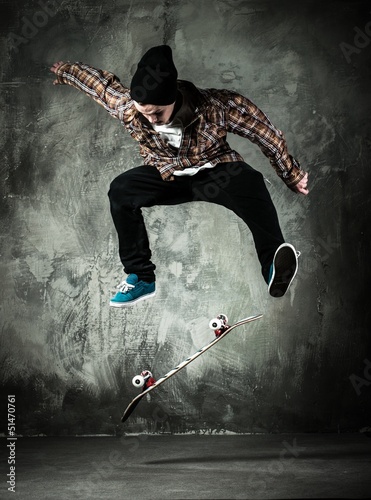 Fototapeta na wymiar Young man in hat and shirt performing stunt on skateboard