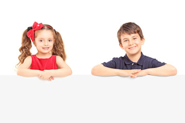 Wall Mural - Little smiling boy and girl standing behind a blank panel