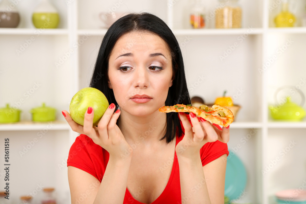 Pretty girl selects pizza or diet on kitchen background