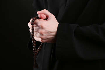 Wall Mural - Priest holding rosary, on black background