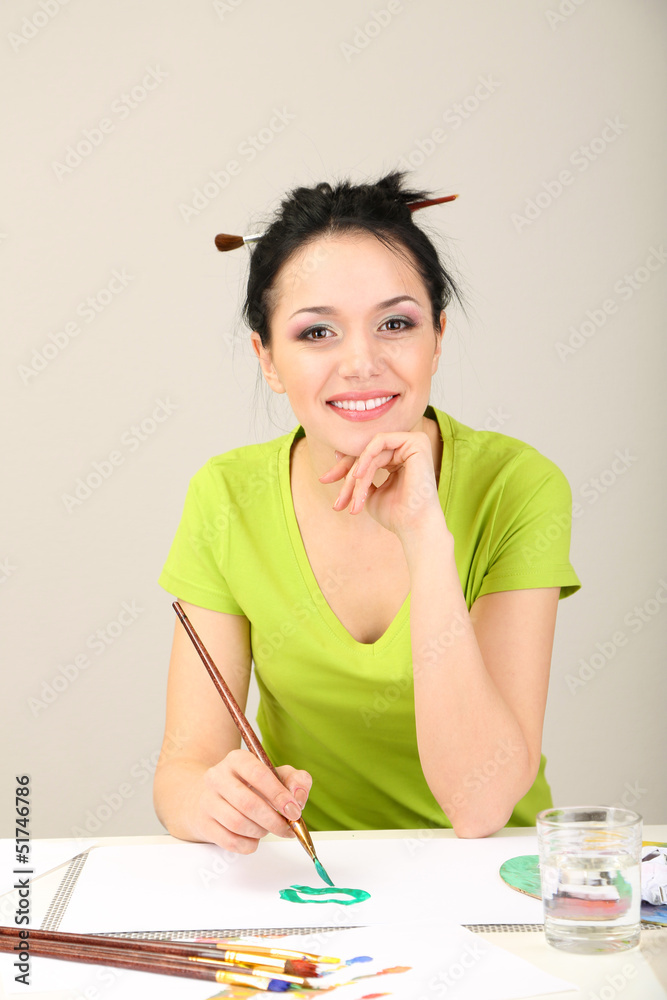 Beautiful young woman painter at work, on color background