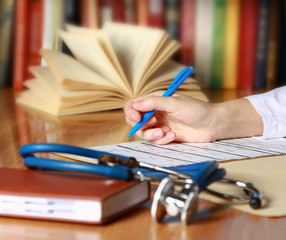 Close-up of writing doctor's hands on a wooden desk