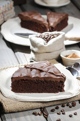 Poster - Chocolate cake on white plate, on hessian. Coffee beans on woode