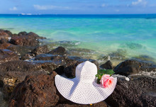 The Rose And Straw Hat Lies On Stones On The Sea  Background..