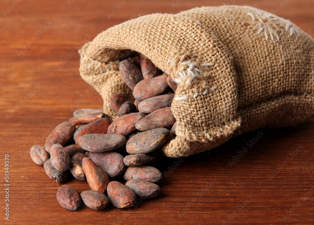 Cocoa beans in bag on wooden background