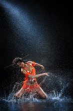 Woman Dancing Under Rain In Orange Dress. Studio