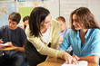 © Monkey Business - Teacher Helping Female Pupil Studying At Desk In Classroom