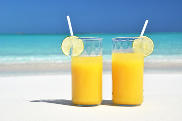 Wall Mural - Two glasses of orange juice on the sandy beach