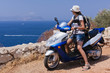 Young woman on a scooter is looking on blue Mediterranean sea.