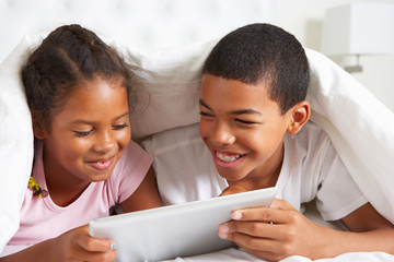 Canvas Print - Two Children Using Digital Tablet Under Duvet