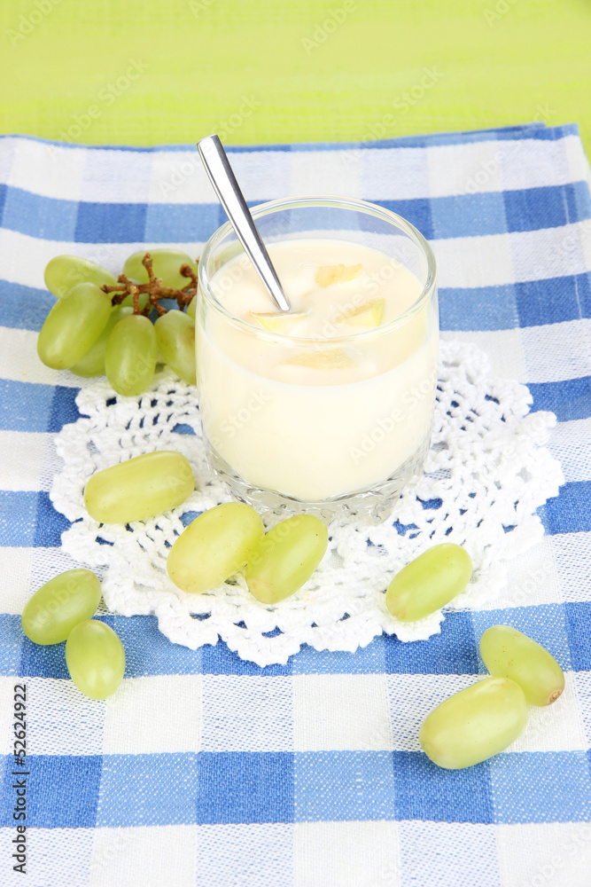 Delicious yogurt in glass with grapes on blue tablecloth