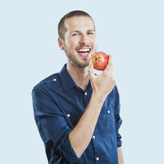 Cheerful beautiful man eating apple, isolated over white backgro