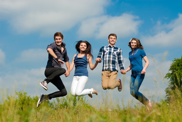 Wall Mural - Four happy teenage friends jumping high in blue sky