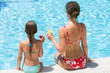 © Pavel Losevsky - Mother and daughter sitting on edge of pool with drink