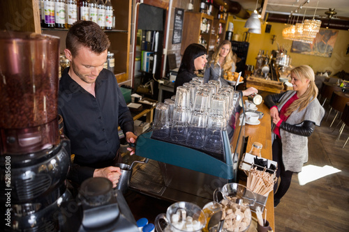 Fotografie, Obraz Bartender Working At Counter While Female Colleague Serving Coff