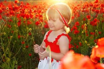 Smiling little girl in red poppies filed, sunset. Outdoors portr