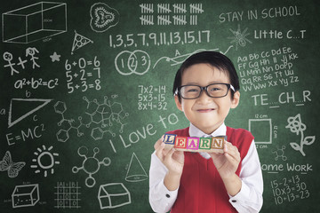 Cheerful boy student holding LEARN block
