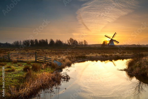 Fototapeta na wymiar windmill during sunrise reflected in river