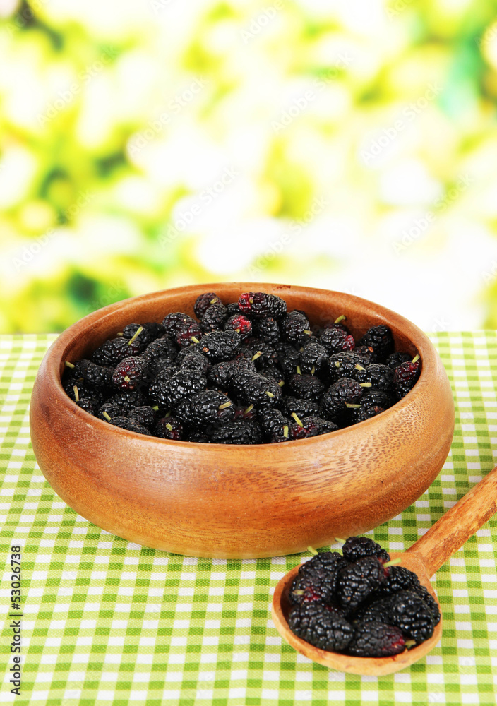 Ripe mulberries in bowl on table on bright background