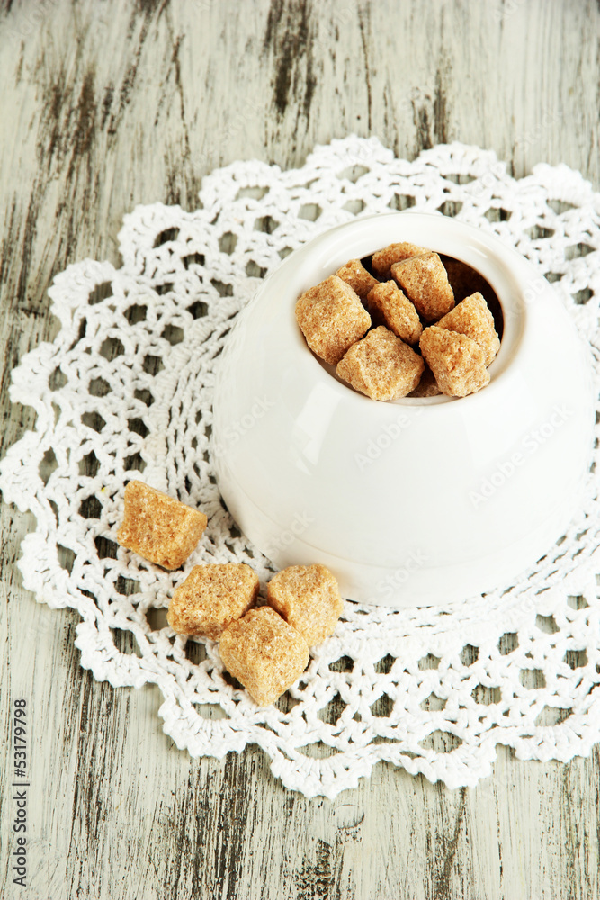 Unrefined sugar in white sugar bowl on wooden background
